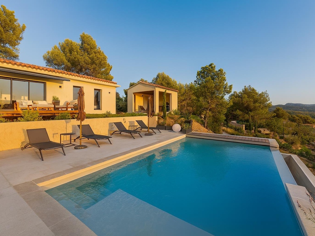 Magnifique villa moderne avec piscine à débordement offrant une vue panoramique sur les collines, dotée d'une terrasse ensoleillée avec chaises longues et un décor méditerranéen.