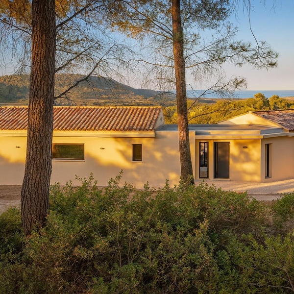 Belle villa méditerranéenne avec toit en tuiles orangées, murs blancs et vue sur la campagne et la mer, nichée parmi les pins parasols.