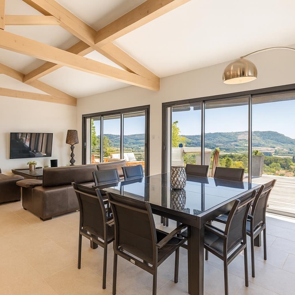 Superbe espace de vie lumineux avec salle à manger moderne, salon confortable et grandes baies vitrées offrant une vue panoramique spectaculaire sur les collines environnantes.